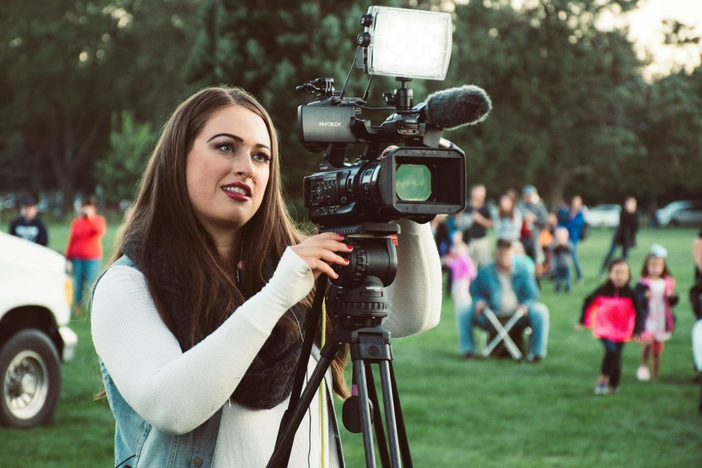 A female videographer operates a professional camera outdoors, capturing live events with precision.
